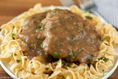 a white plate topped with meat and noodles covered in gravy on top of a wooden table