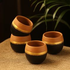 three brown and black vases sitting on top of a table next to a plant