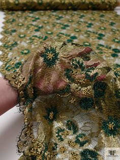 a woman's hand is holding onto a gold and green lace fabric with flowers on it