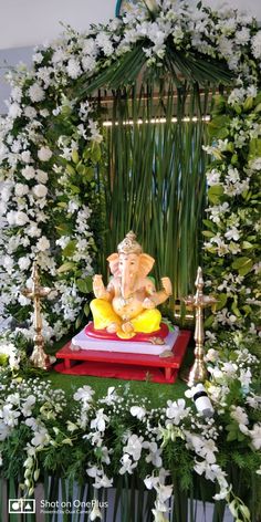 an elephant statue sitting on top of a red platform surrounded by flowers and greenery