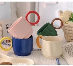 there are many different colored mugs on the table next to some books and other items