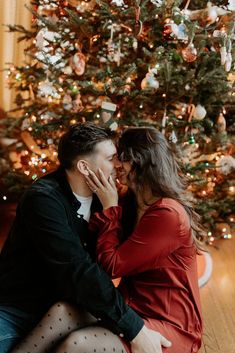 a man and woman sitting in front of a christmas tree with their arms around each other