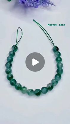 a green beaded bracelet sitting on top of a white table next to purple flowers