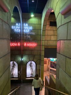 a woman is walking down an escalator in a building with neon signs on the walls