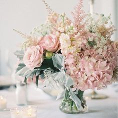 a vase filled with pink and white flowers on top of a table next to candles