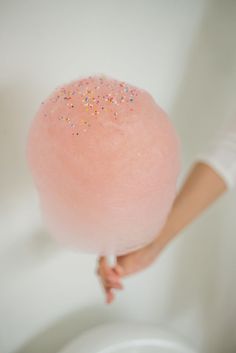 a person holding a large pink ball of cotton candy in their right hand and the other hand is pointing at it