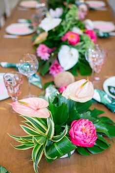 the table is set with pink flowers and green leaves, along with place settings for dinner