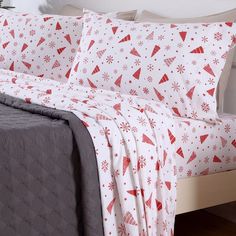 a bed covered in white and red sheets with christmas trees on them, next to a night stand