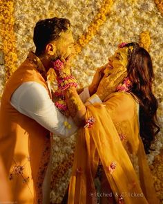 a man and woman standing next to each other in front of a flower wall covered with petals