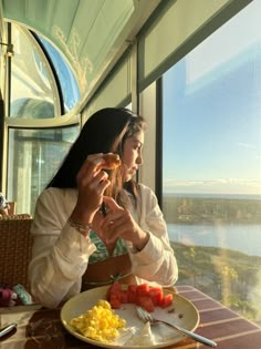 two women sitting at a table with food in front of them and looking out the window