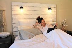 a woman laying in bed reading a book with lights on the headboard behind her