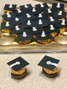 graduation cap cookies are arranged on a tray with white ribbon and gold foiled cupcakes