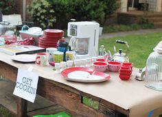 a table with plates and cups on it in front of a house that has been set up for an outdoor cooking event