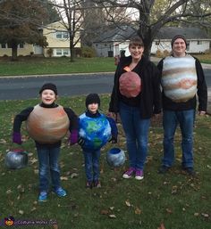 three adults and two children in costumes standing on the grass with balls around their necks