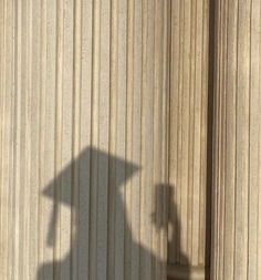 the shadow of a person with a hat on their head is seen in front of a building