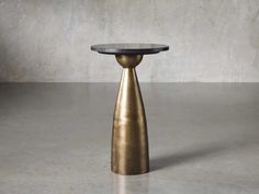 a round table with a black top and gold base on a concrete floor in front of a gray wall