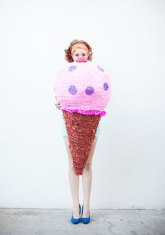 a woman wearing an ice cream cone costume with polka dots on her face, standing in front of a white wall