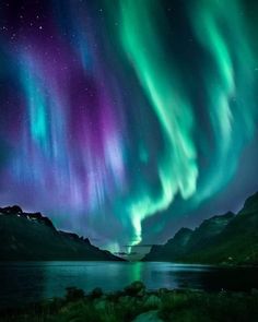 an aurora bore is seen in the night sky over water and mountains with green lights