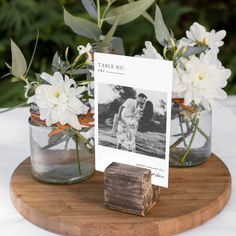 two mason jars with flowers in them are on a wooden stand next to a card