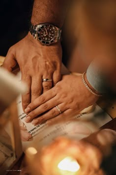 two people holding hands over a paper with a candle in the background on a table