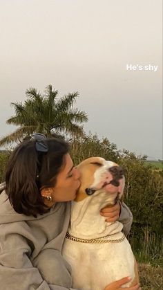 a woman is kissing her dog on the nose with palm trees in the back ground