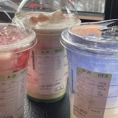 three plastic cups filled with liquid sitting on top of a metal table next to each other