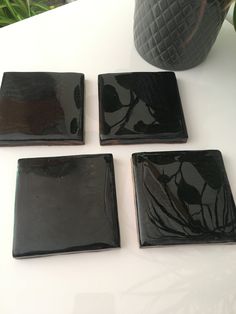 four black square plates sitting on top of a white table next to a potted plant