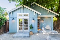 a small blue house with white trim on the front door and windows, sitting next to a tree