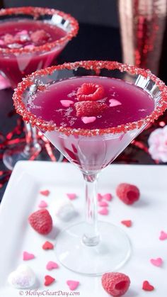 two martinis with raspberries in them on a white plate and pink confetti