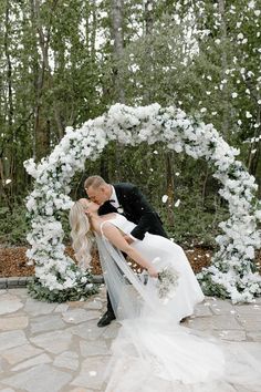 a bride and groom kissing in front of a white floral arch