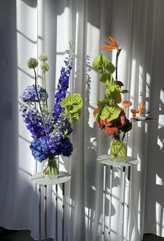 two vases with flowers are sitting in front of a window, one is blue and the other is orange