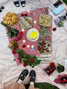 a picnic blanket with food on it and flowers in the grass next to some people's feet