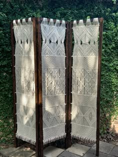 two white woven screens sitting next to each other on top of a stone floor in front of a green bush