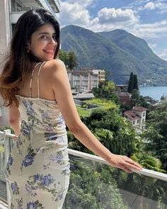 a woman standing on a balcony next to a lake and mountains with her arms out