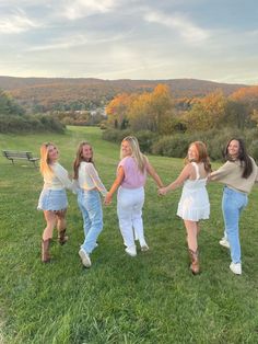 four girls are holding hands and walking in the grass