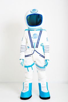 an astronaut in white and blue space suit with goggles on his head, standing against a white wall