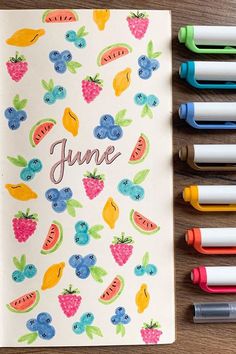 an open notebook with fruit and berries on it, surrounded by markers that read june