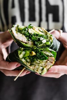 two people holding food wrapped in leafy greens and other vegetables, with chopsticks sticking out of the wrap