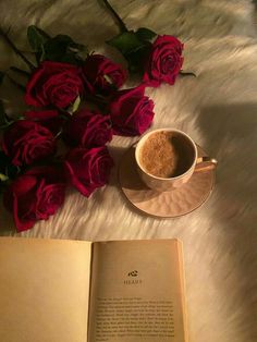 a cup of coffee next to a book and some red roses on a fur surface