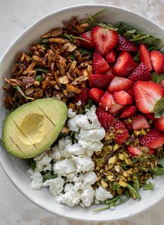 a white bowl filled with strawberries, avocado, nuts and feta cheese