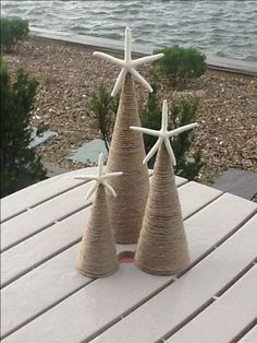 three small trees made out of twine with starfish on top, sitting on a table next to the ocean