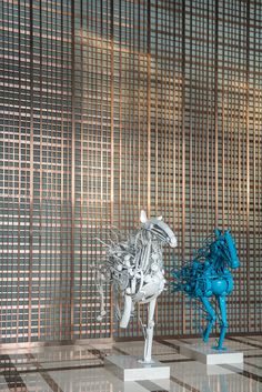 two sculptures on pedestals in front of a wall with woven squares and lines behind them