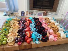 a wooden table topped with lots of fruit and crackers next to a fire place