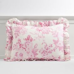 a pink and white pillow with ruffles on the bottom, in front of a wall