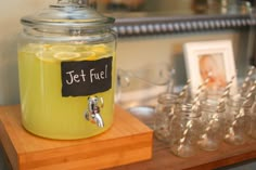 a glass jar filled with lemonade sitting on top of a wooden table next to wine glasses