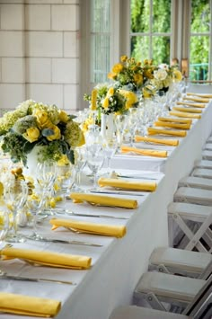 a long table with yellow napkins and white vases filled with flowers on it