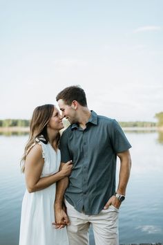 a man and woman standing next to each other near the water with their eyes closed