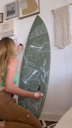 a woman writing on a wall next to a surfboard with flowers and leaves drawn on it