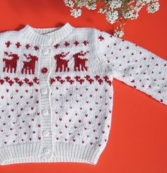 a knitted sweater with red and white deers on it, next to flowers