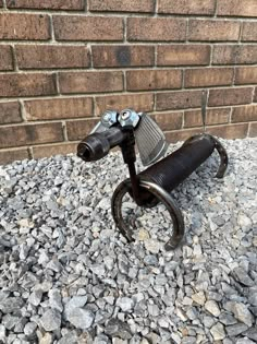 an old fashioned scooter is sitting on the gravel near a brick wall,